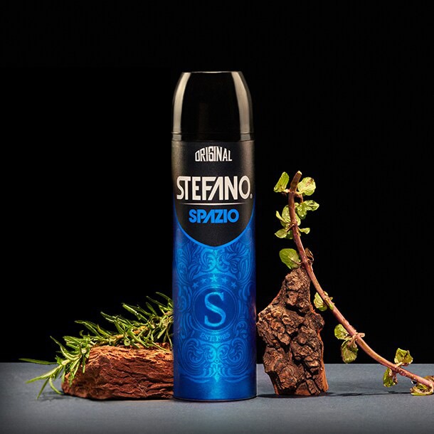 Un desodorante en aerosol Stefano Spazio sobre un fondo negro, con pimienta negra, madera y flores de lavanda.