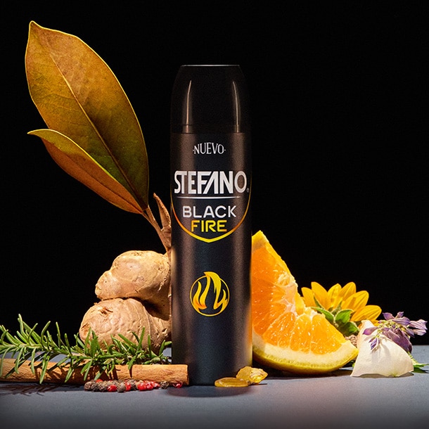 Un envase de desodorante en aerosol Stefano Black Fire en el centro, acompañado de jengibre, rodajas de naranja, una rama de romero, una rama de canela, granos de pimienta y hojas secas sobre un fondo negro.